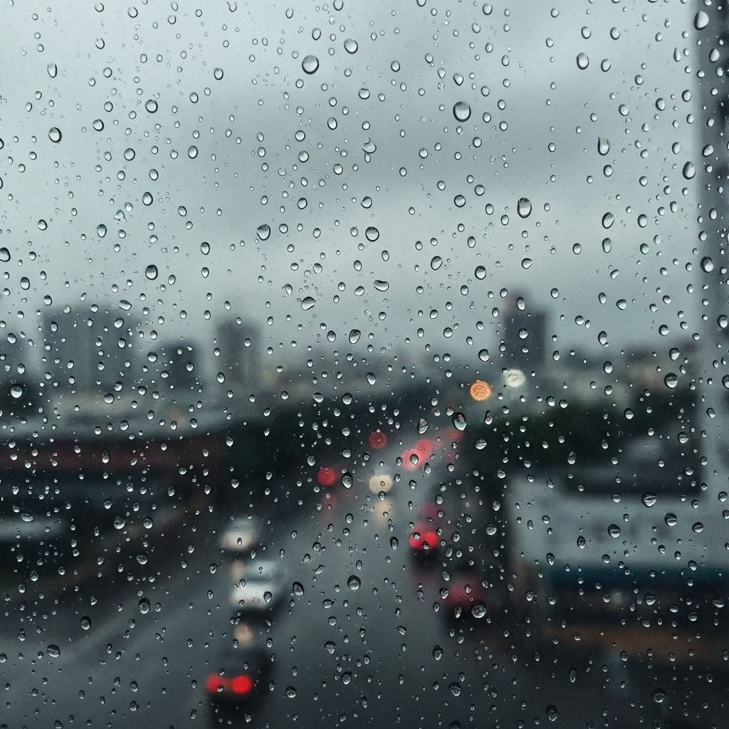 Rain-streaked window with blurred urban view, contemplative mood